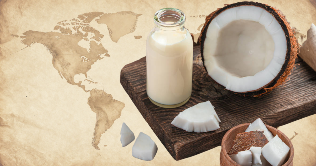 Botella de leche de coco junto a trozos y una mitad de coco sobre una tabla de madera, con mapa antiguo de América al fondo, representando el origen y expansión mundial de la leche de coco en la cocina.